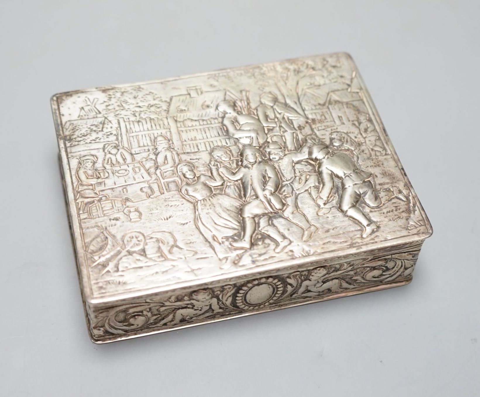 A late 19th / early 20th century German Hanau silver rectangular box and cover, the top embossed with a scene of revellers, import marks for London, 1912, 11.7cm.